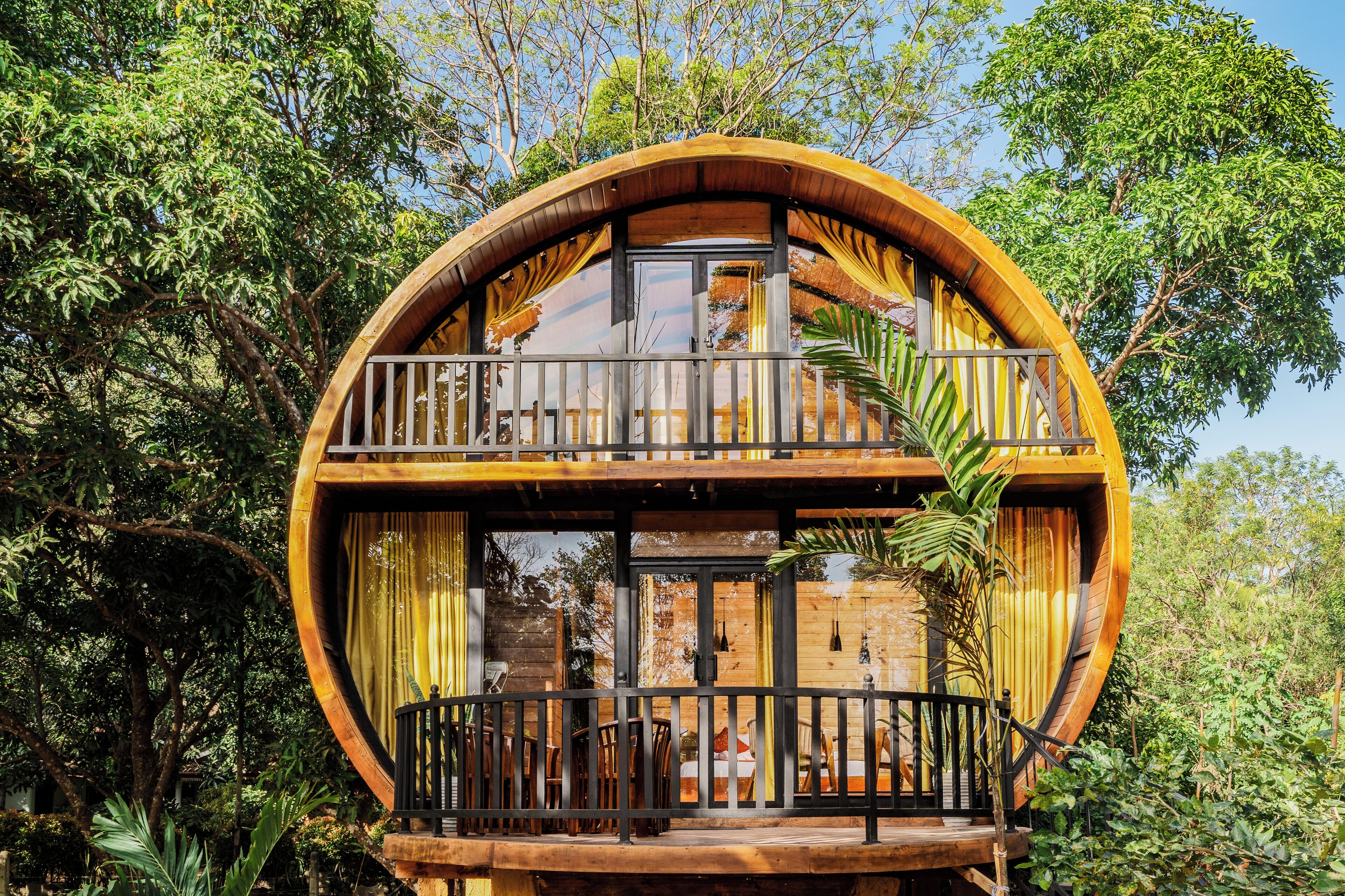 A circular wooden structure with a balcony, surrounded by lush greenery.