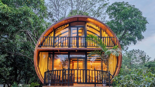 Estructura redonda de madera con un balcón, rodeada de abundante vegetación.