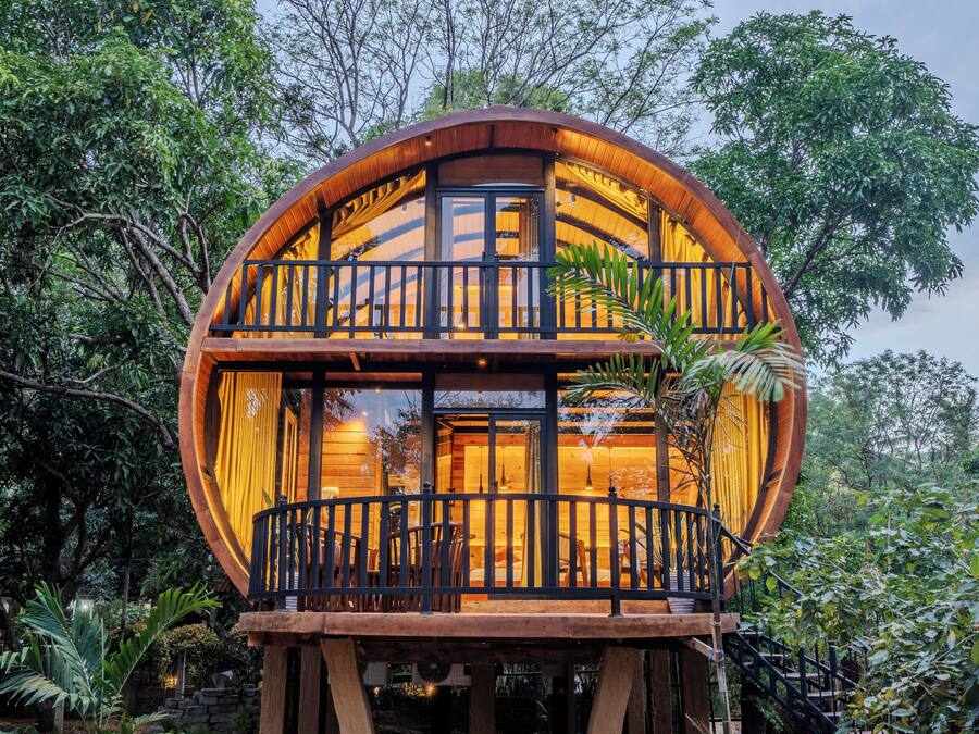 A round, wooden structure with a balcony, surrounded by lush greenery.