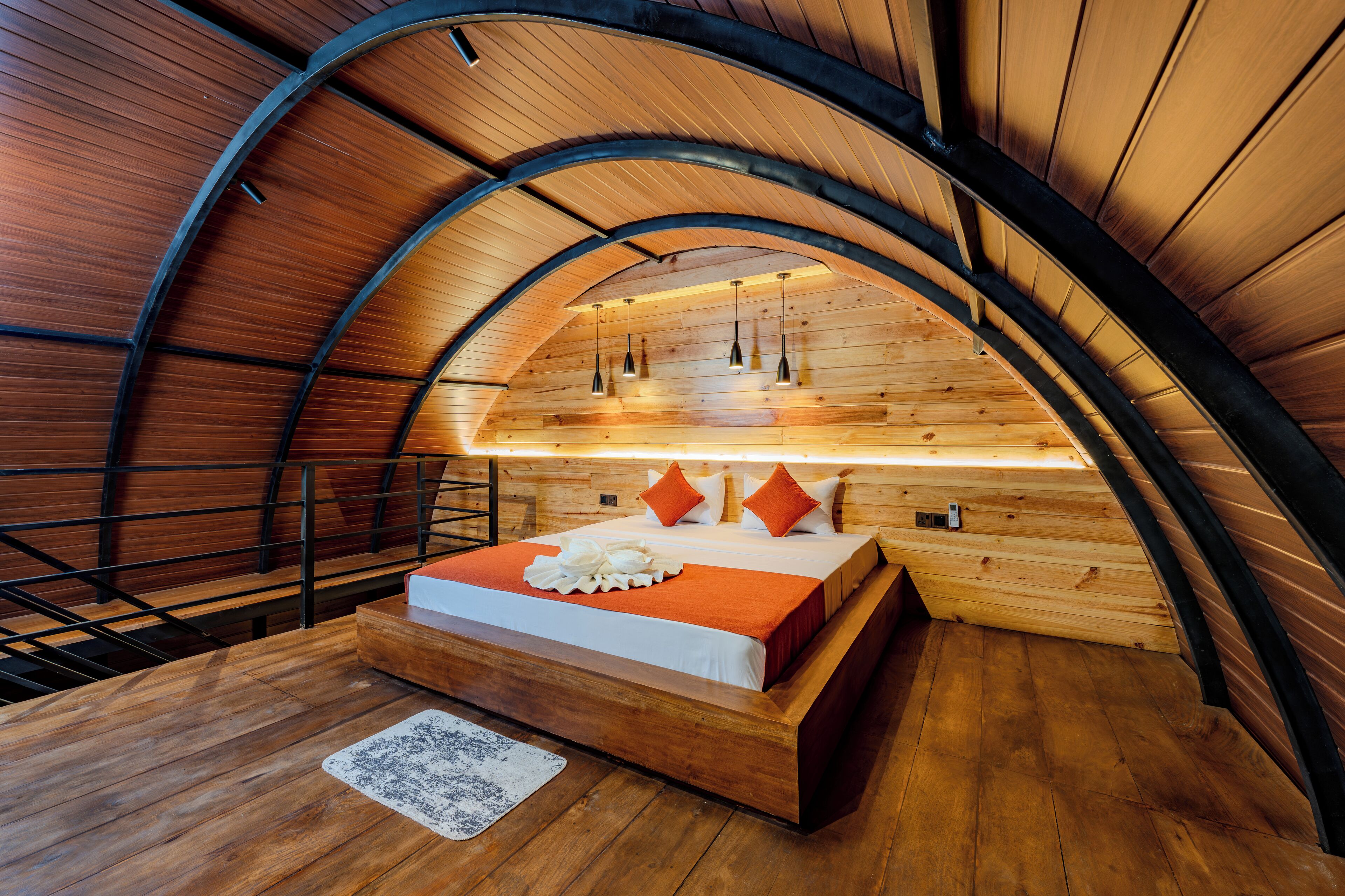 Une chambre avec un plafond en bois, un lit recouvert d’une courtepointe blanche et orange, et un plancher en bois.