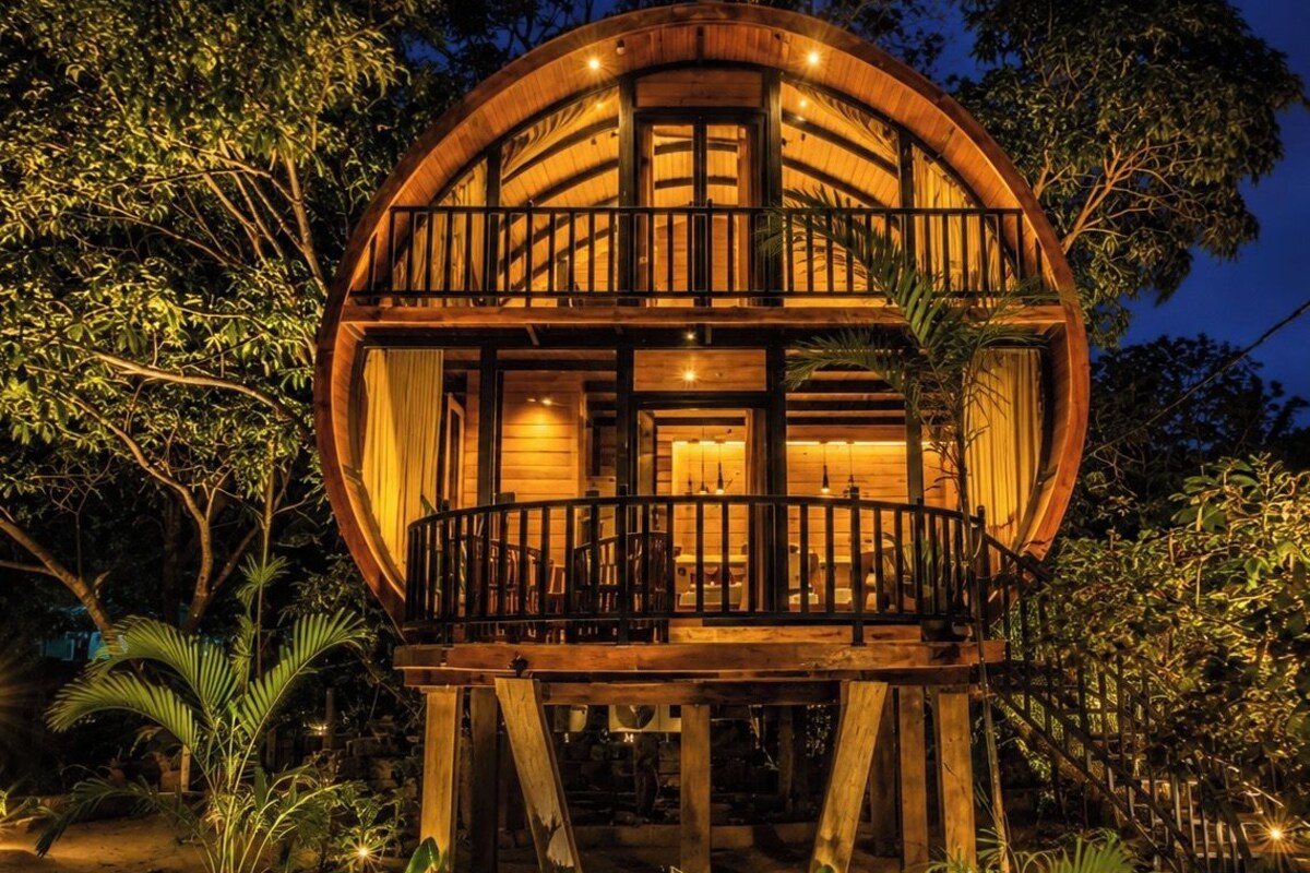 Een houten, rond gebouw met een balkon, omringd door begroeiing.
