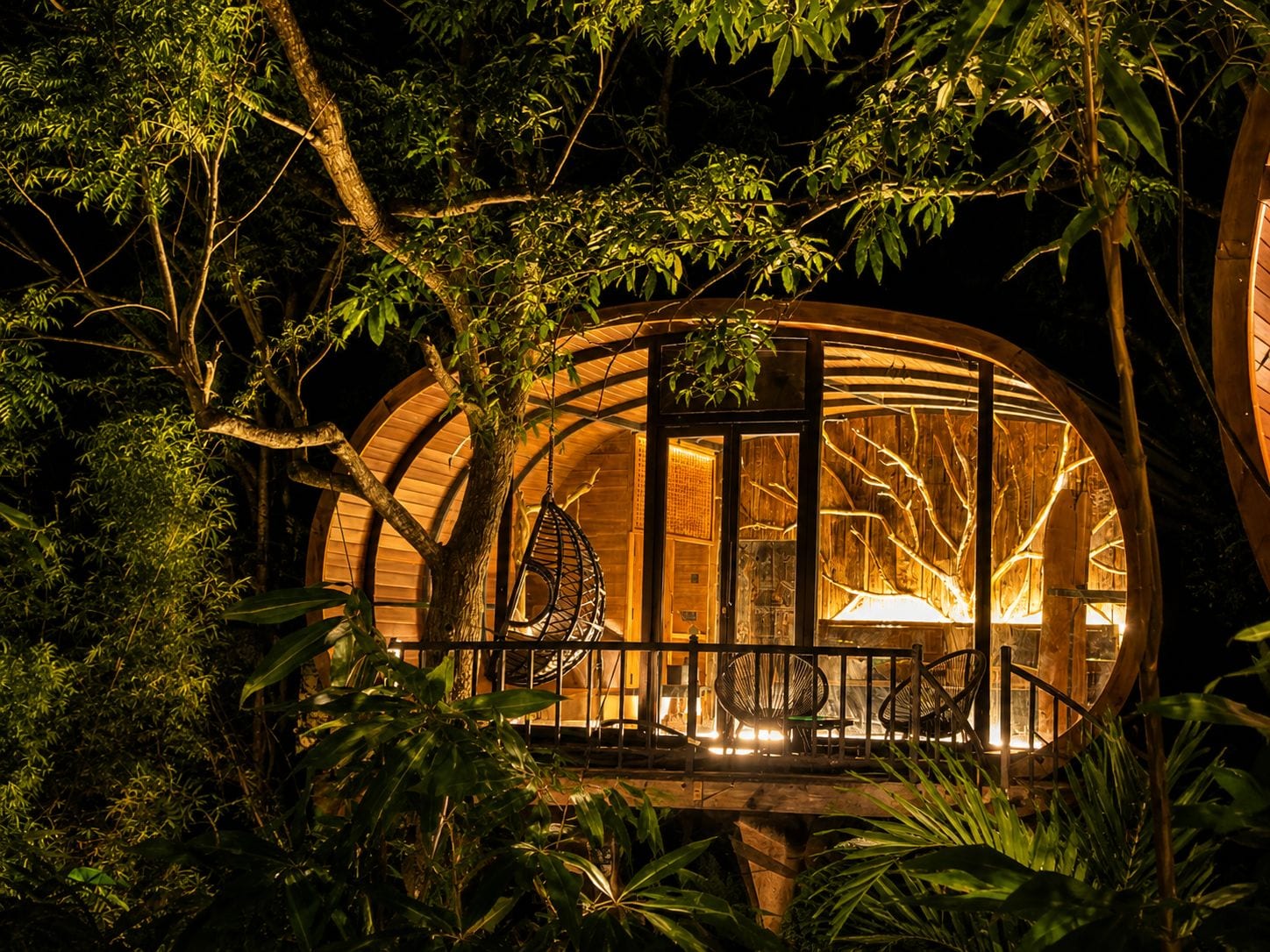 A treehouse with a circular wooden structure, a hammock, and a seating area with chairs.