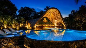 A swimming pool with a unique architectural structure in the background, surrounded by trees.