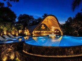 Una piscina con una estructura arquitectónica singular al fondo, rodeada de árboles.