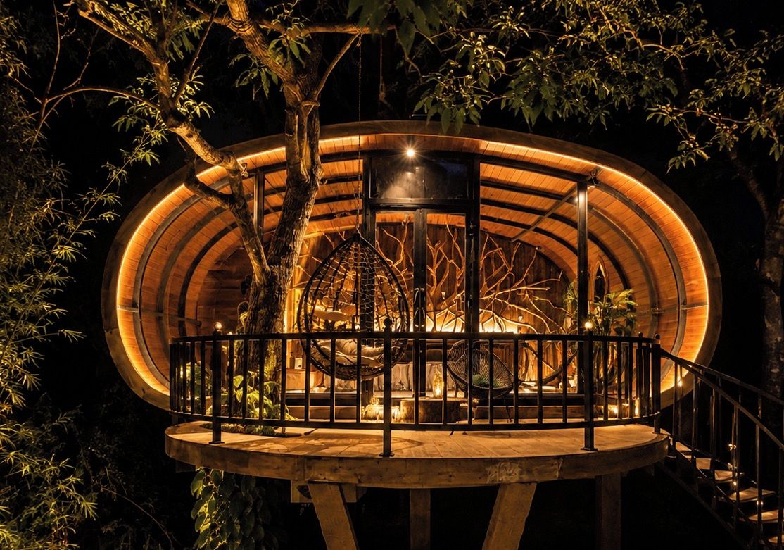 Una estructura circular de madera con balcón, rodeada de árboles.