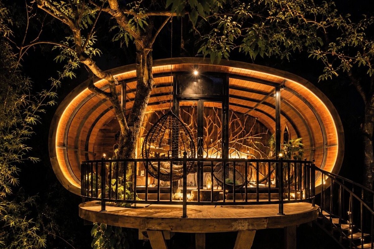 Een ronde houten constructie met een balkon, omringd door bomen.
