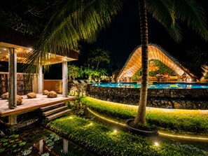 A nighttime resort with a swimming pool, outdoor seating, and a thatched-roof structure. - Woodland Sanctuary (Habarana)