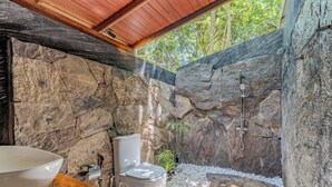 Un baño con paredes de piedra, un inodoro, un lavabo y una ducha.