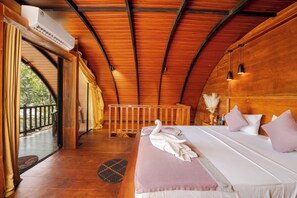 Een kamer met een houten plafond, een bed met een witte dekbedovertrek en kussens, een handdoek in de vorm van een zwaan, en een balkon met uitzicht.