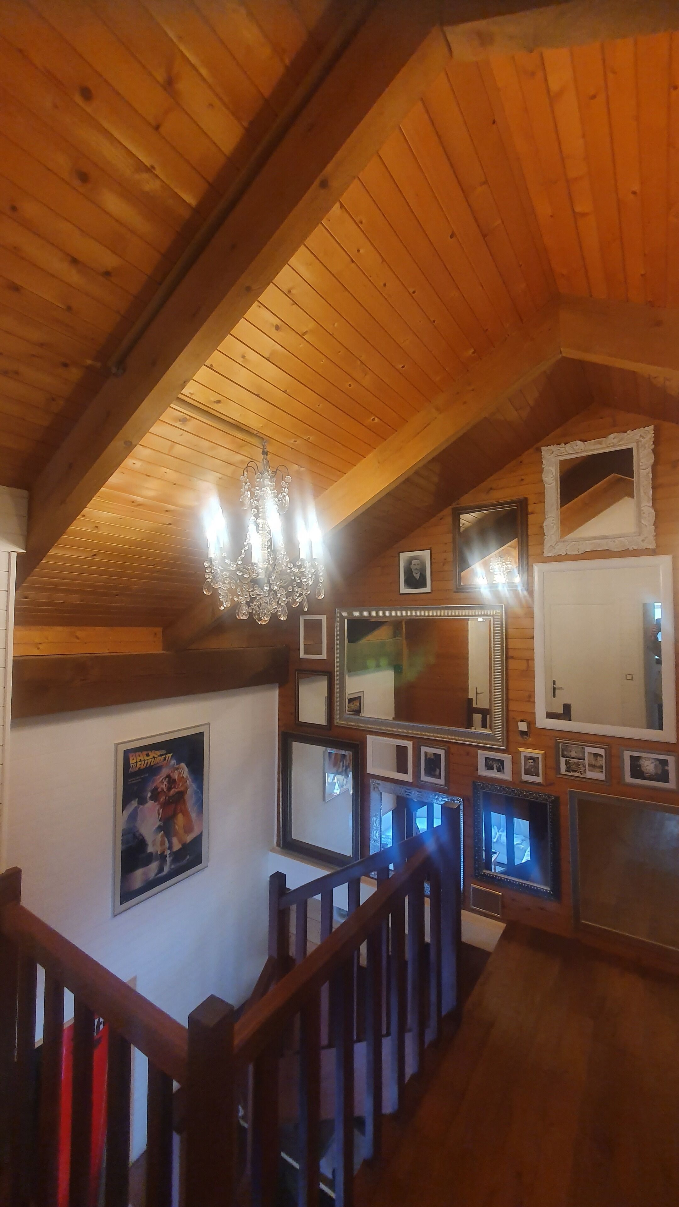 Een houten interieur met een kroonluchter, meerdere ingelijste foto's en een trap.
