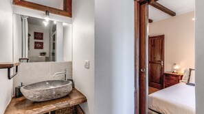 Ein Badezimmer mit einem Steinkonstruktion Waschbecken, einem Spiegel und einer Holztür, die zum Schlafzimmer führt.
