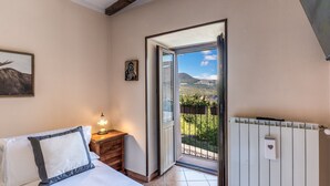 Une chambre à coucher avec un lit, une table de chevet, une lampe et une vue sur un balcon donnant sur un paysage montagneux.