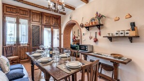 Un coin repas rustique, avec des meubles en bois, une arche en briques et un espace cuisine doté d’étagères et de bocaux.