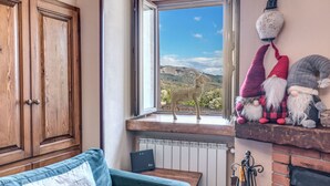 Une pièce chaleureuse avec un meuble en bois, un canapé bleu, une fenêtre donnant sur une montagne et une étagère ornée de petits gnomes décoratifs.