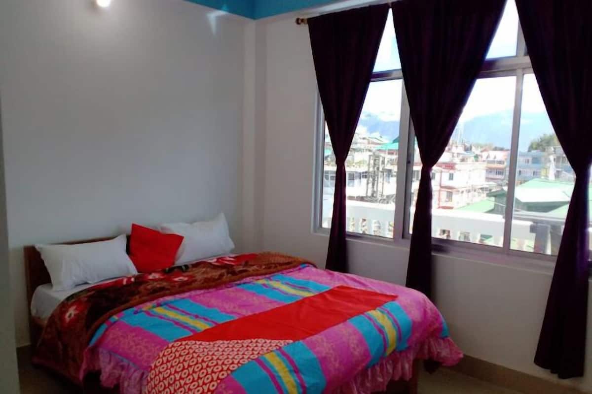 Quarto com cama, janela com cortinas e vista para edifícios.