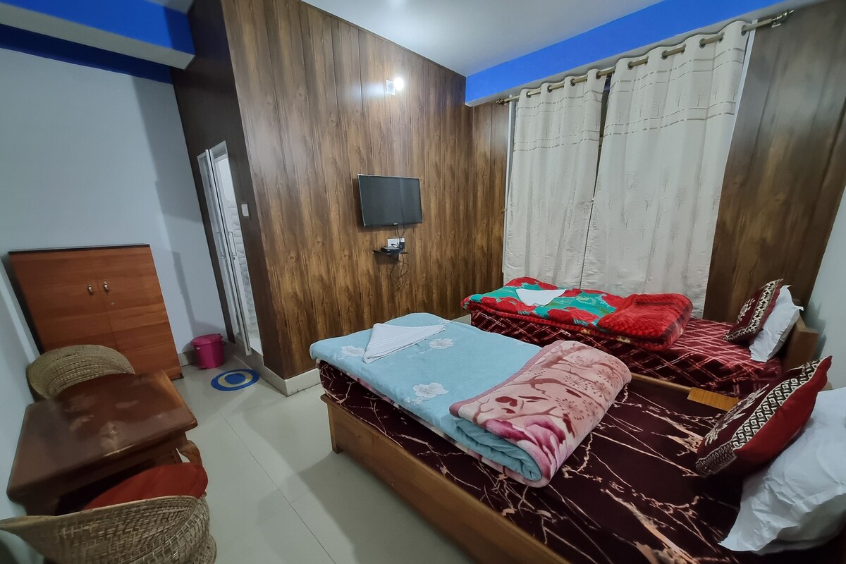A bedroom with two beds, a wooden wardrobe, a television, and a small table.