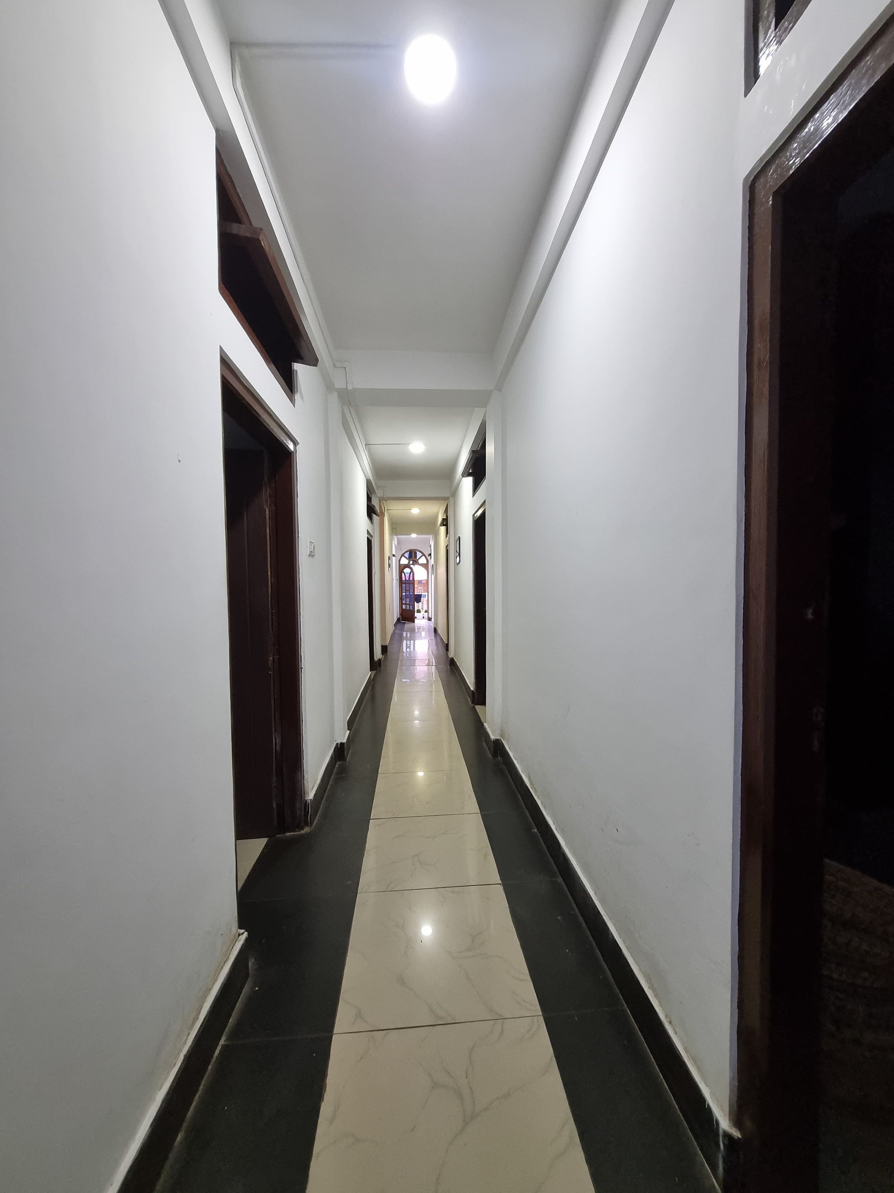 A corridor with a tiled floor, white walls, and doors on both sides.