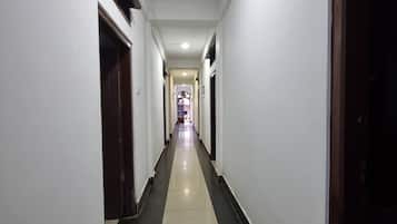 En gang med flisegulv, hvide vægge og døre på begge sider.