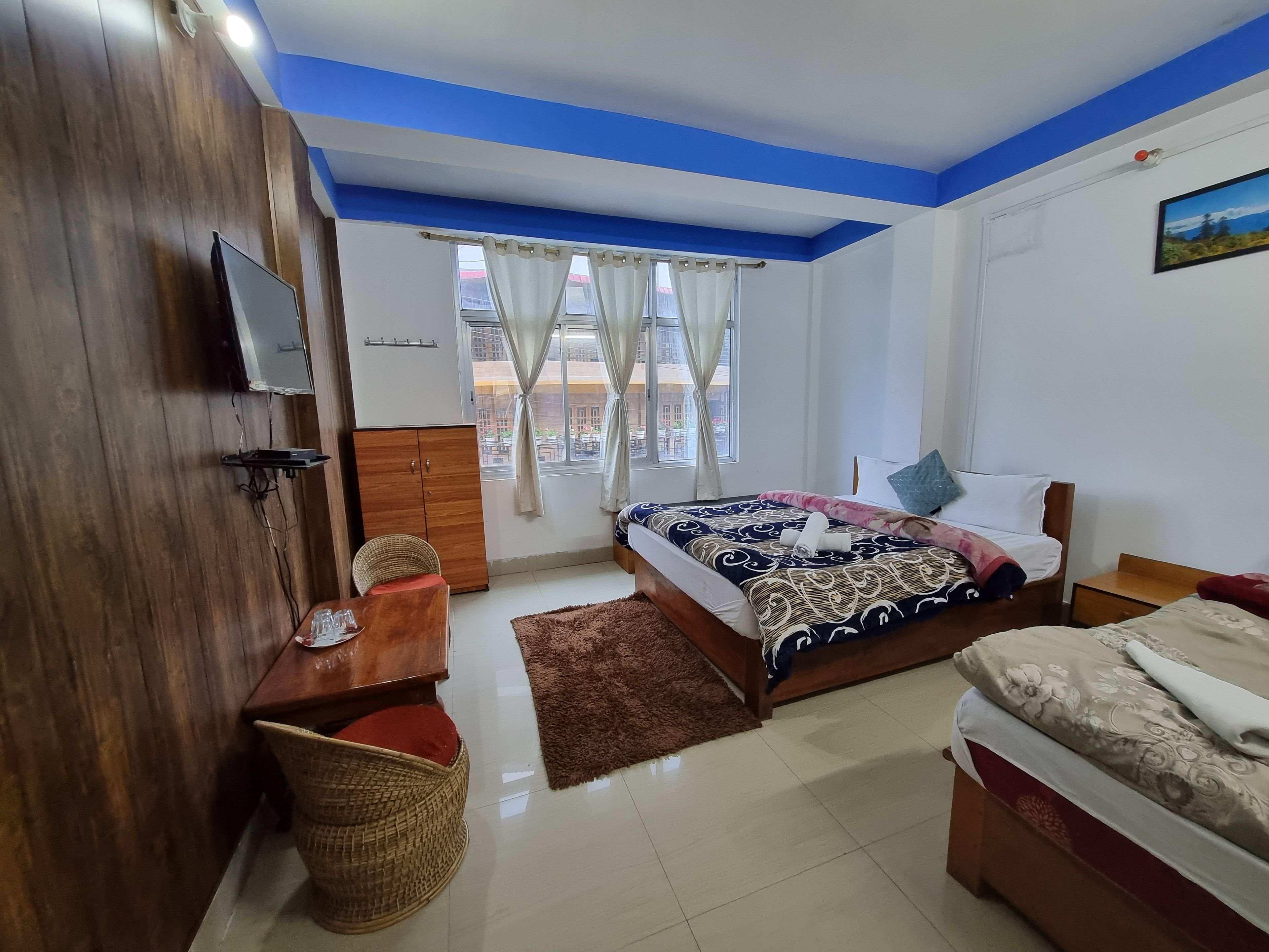 A bedroom with a bed, a desk, a television, and a window with curtains.