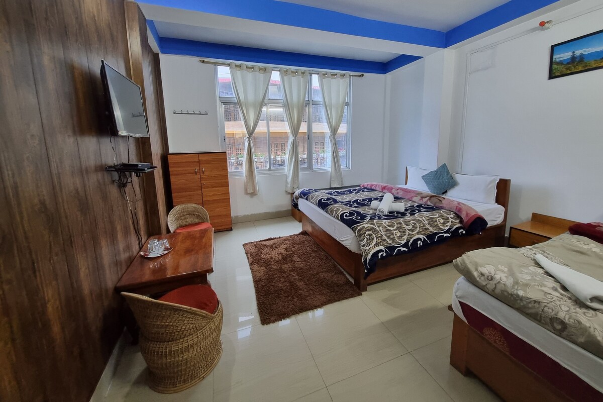 A bedroom with a bed, a desk, a television, and a window with curtains.