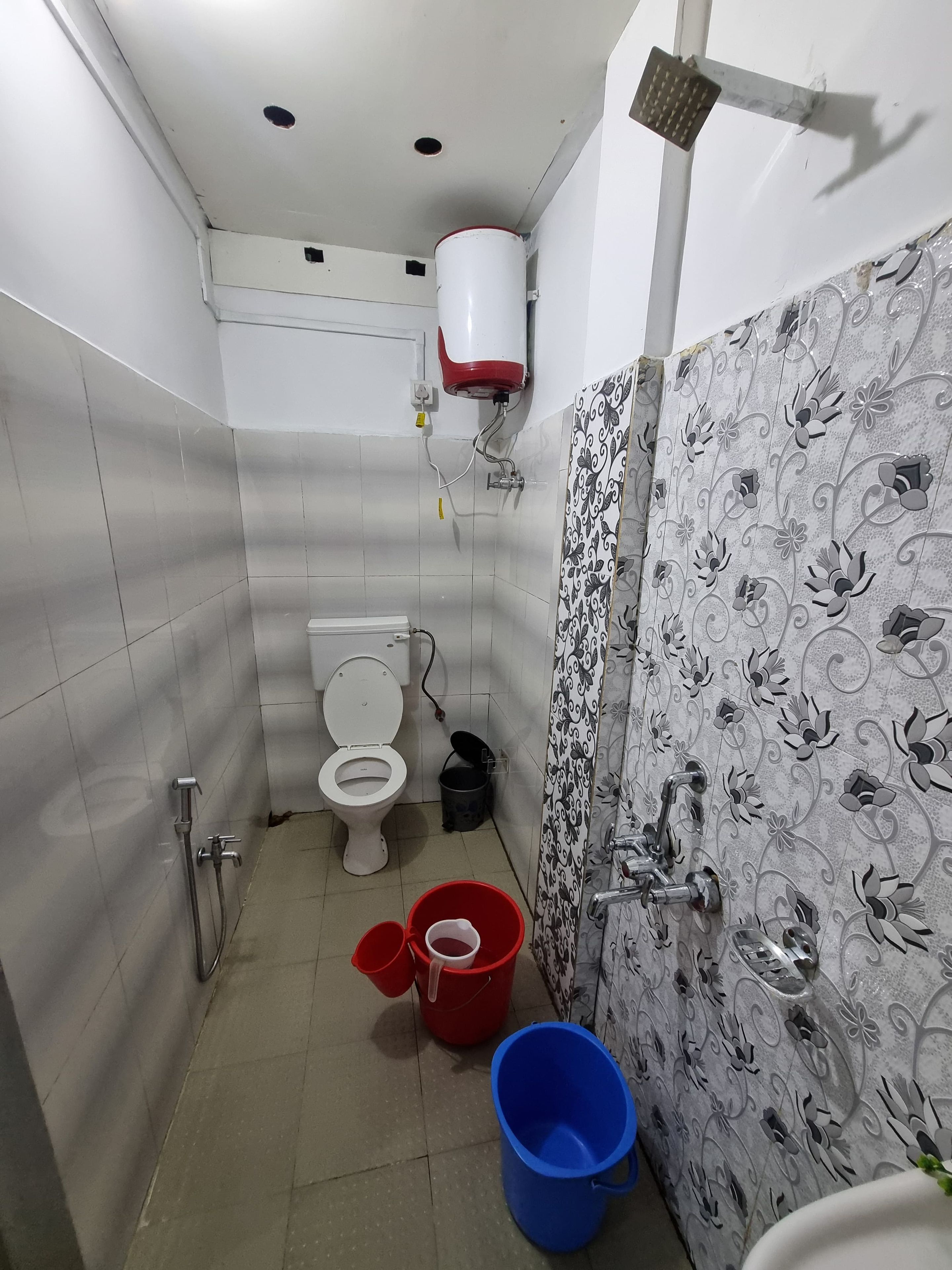 Ein Badezimmer mit Toilette, Dusche und einem roten Eimer auf dem Boden.
