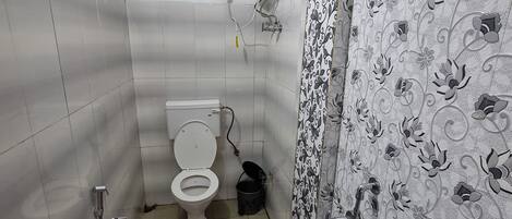 Ein Badezimmer mit Toilette, Dusche und einem roten Eimer auf dem Boden.