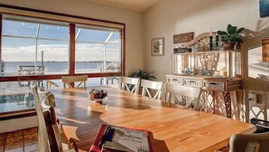 Un coin repas avec une table en bois, des chaises blanches et une vue sur la mer, grâce à de grandes fenêtres.