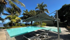 A pool area with lounge chairs and umbrellas, surrounded by palm trees and a view of the ocean. - ANKI LODGE (Nosy Be)
