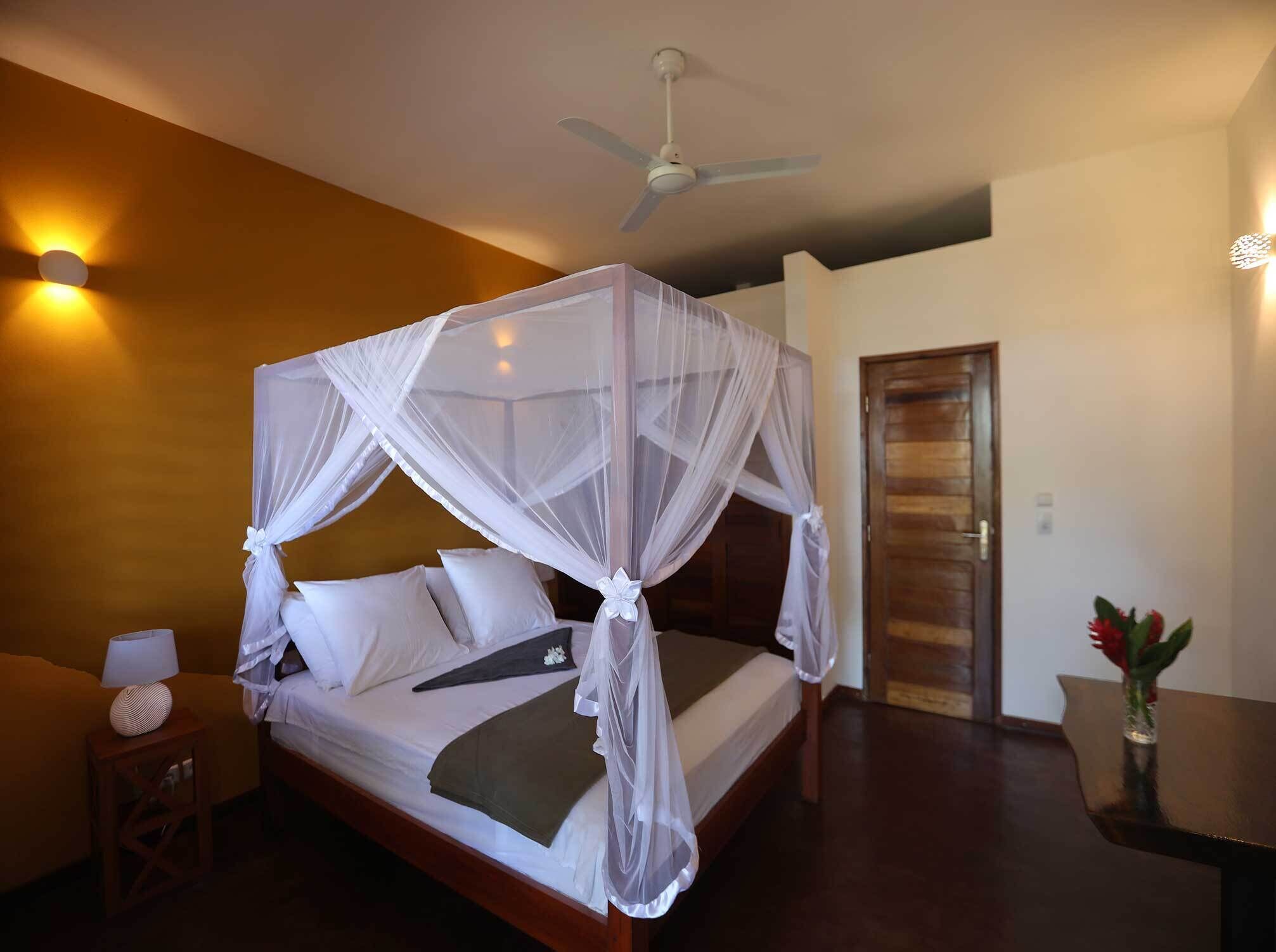 A four-poster bed with a canopy, a ceiling fan, and a bedside table with a lamp.