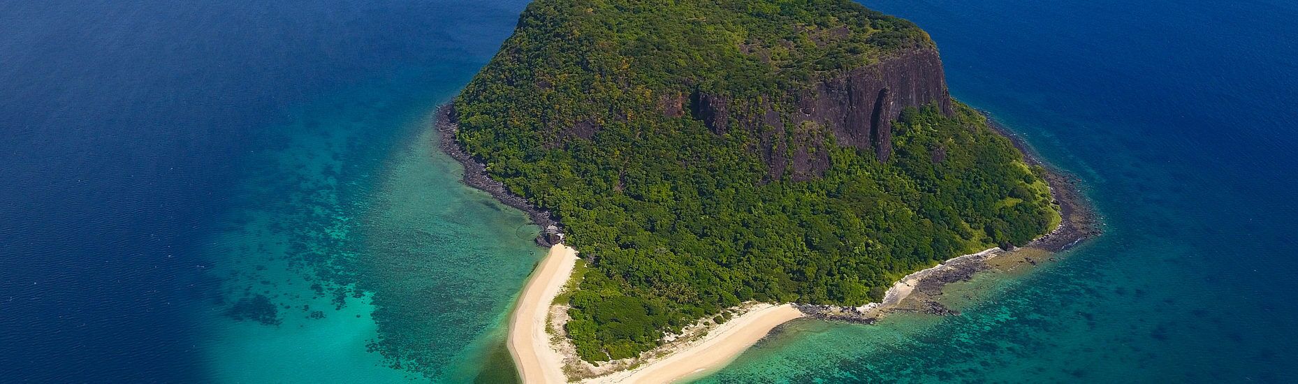 Eine Vogelperspektive einer tropischen Insel mit einem schmalen Strand, dichtem Wald und klarem, blauem Wasser.