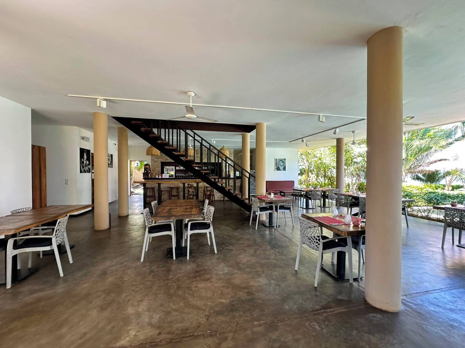 Amplio espacio interior con una escalera central, varias mesas de comedor y sillas.