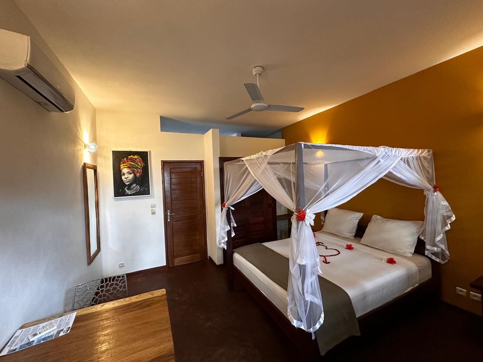 A hotel room with a four-poster bed, a ceiling fan, and a wall-mounted air conditioner.