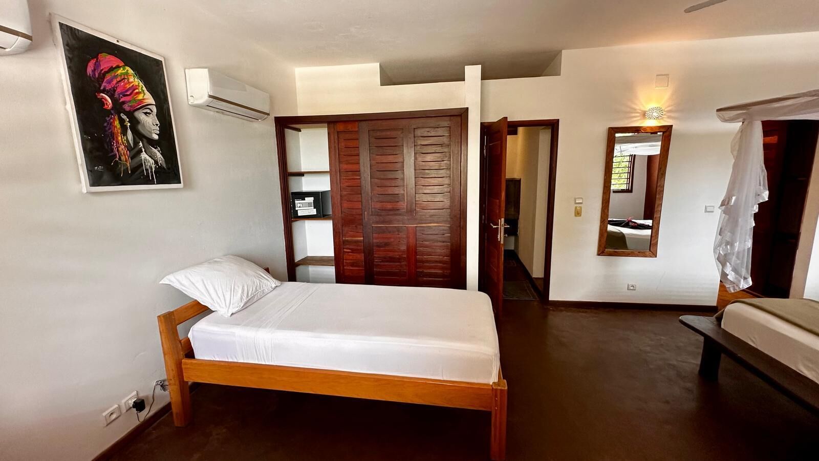 Un dormitorio con cama de madera, un armario, un espejo y aire acondicionado de pared.