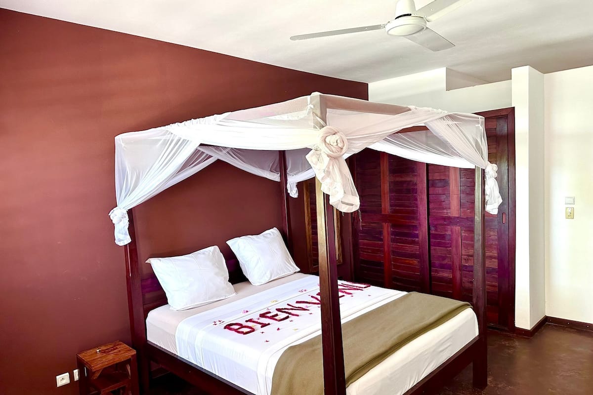 A four-poster bed with a canopy, white bedding, and a 'BIENVENUE' sign.