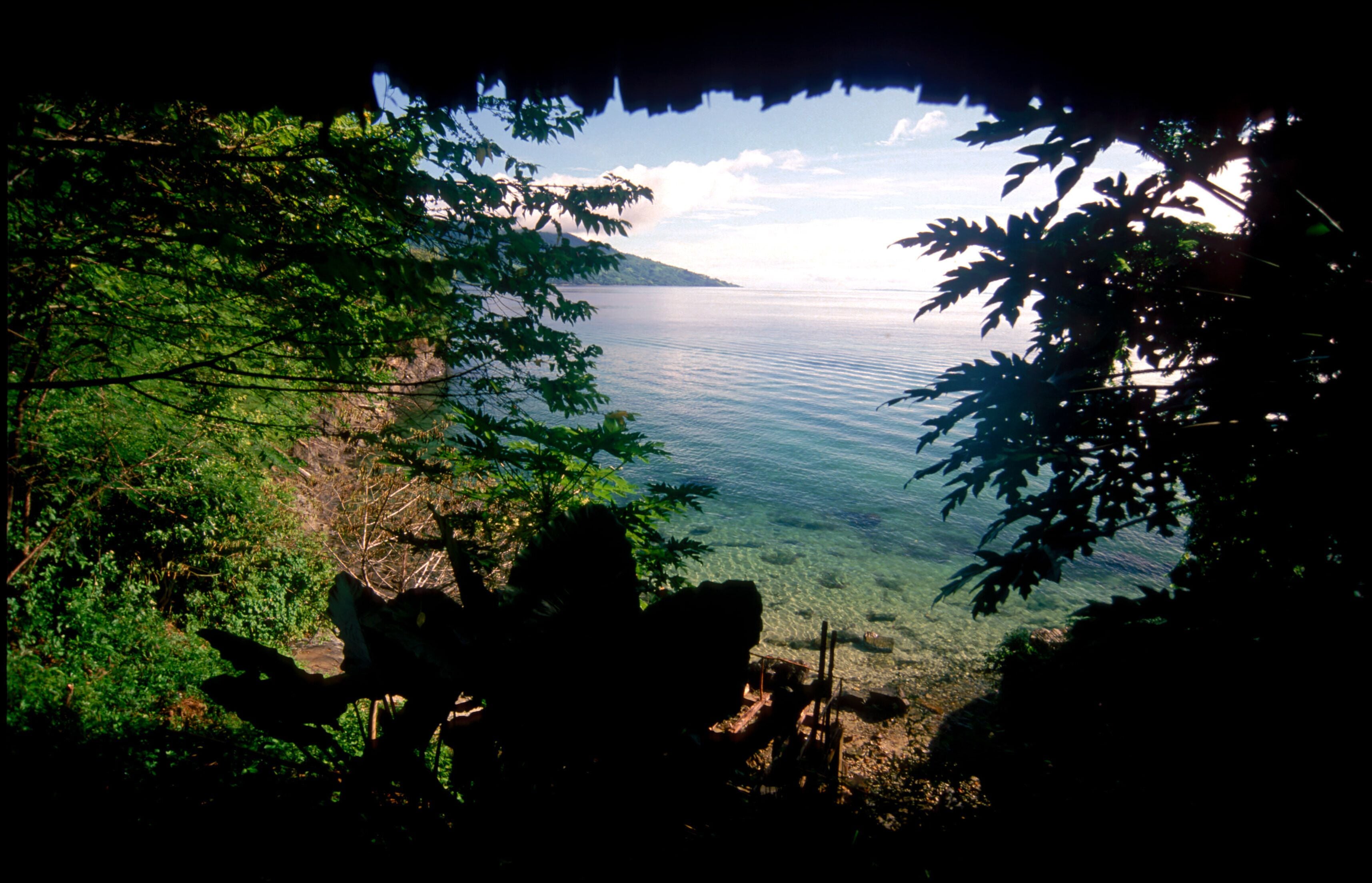 A view through a natural archway with a body of water and a distant landmass.