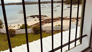 A view through a barred window of a beach with boats, a sandy shore, and a white fence. - Charming 2-bedroom apartment with WiFi, AC in enchanting Port Louis (Port Louis)