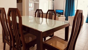 A dining area with a glass-top table and wooden chairs, a television in the background, and a view of the outdoors through a window. - Charming 2-bedroom apartment with WiFi, AC in enchanting Port Louis (Port Louis)