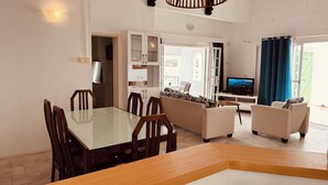 A modern living room with a dining area, a TV, and a large window with curtains. - Charming 2-bedroom apartment with WiFi, AC in enchanting Port Louis (Port Louis)