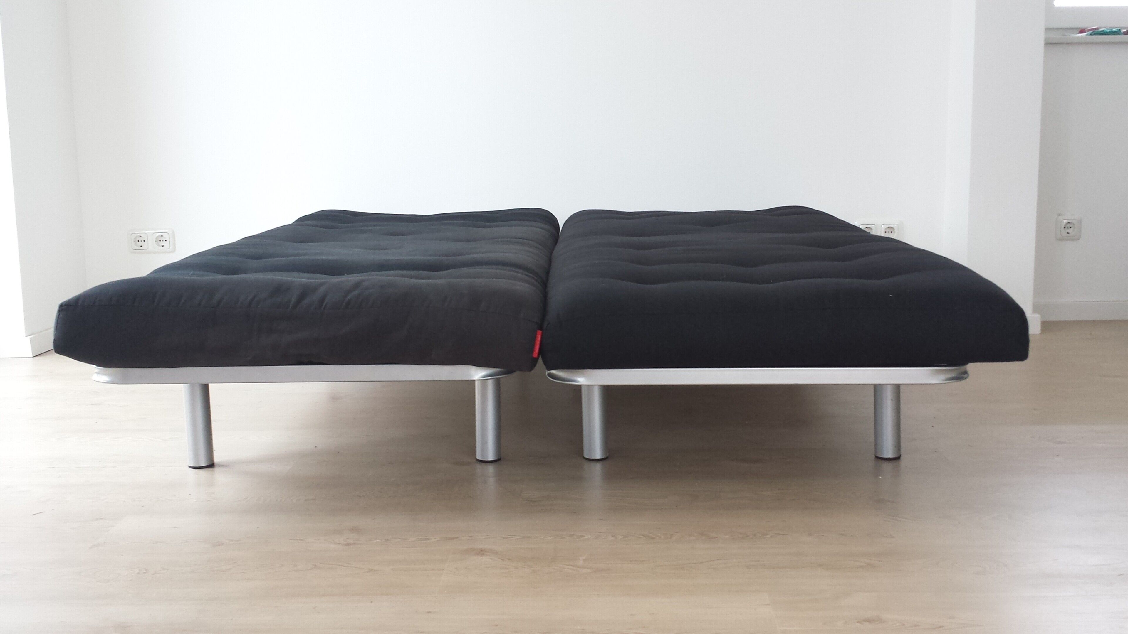 A room with two black upholstered benches on metal legs, a white wall, and a wooden floor.