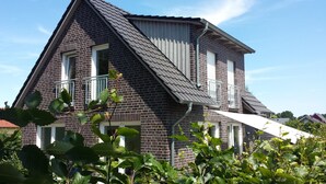 Uma casa de dois andares com telhado íngreme, fachada de tijolos e persianas brancas.