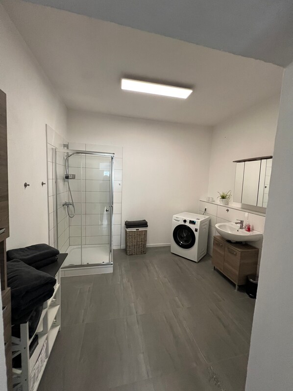 A modern bathroom with a glass shower enclosure, a washing machine, a sink, and a mirror.