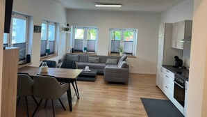 A modern apartment with a dining area, sofa, kitchen, and large windows.
