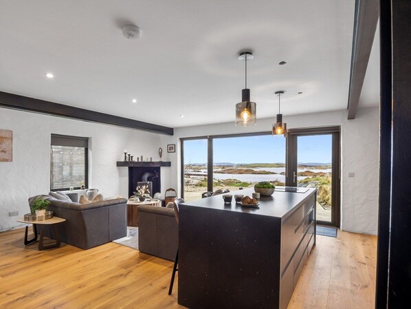 A modern interior with a kitchen island, seating area, and large windows offering a view of the outdoors.