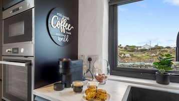 Una cocina moderna con estación de café, que incluye cafetera, tazas y pasteles.