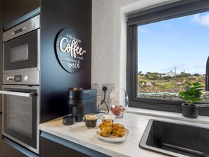 Una cocina moderna con estación de café, que incluye cafetera, tazas y pasteles.