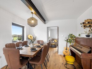 A dining area with a wooden table set for six, surrounded by brown chairs, a hanging light fixture, and a view through a window. - GarraÍ Locha Cottage (Roundstone)