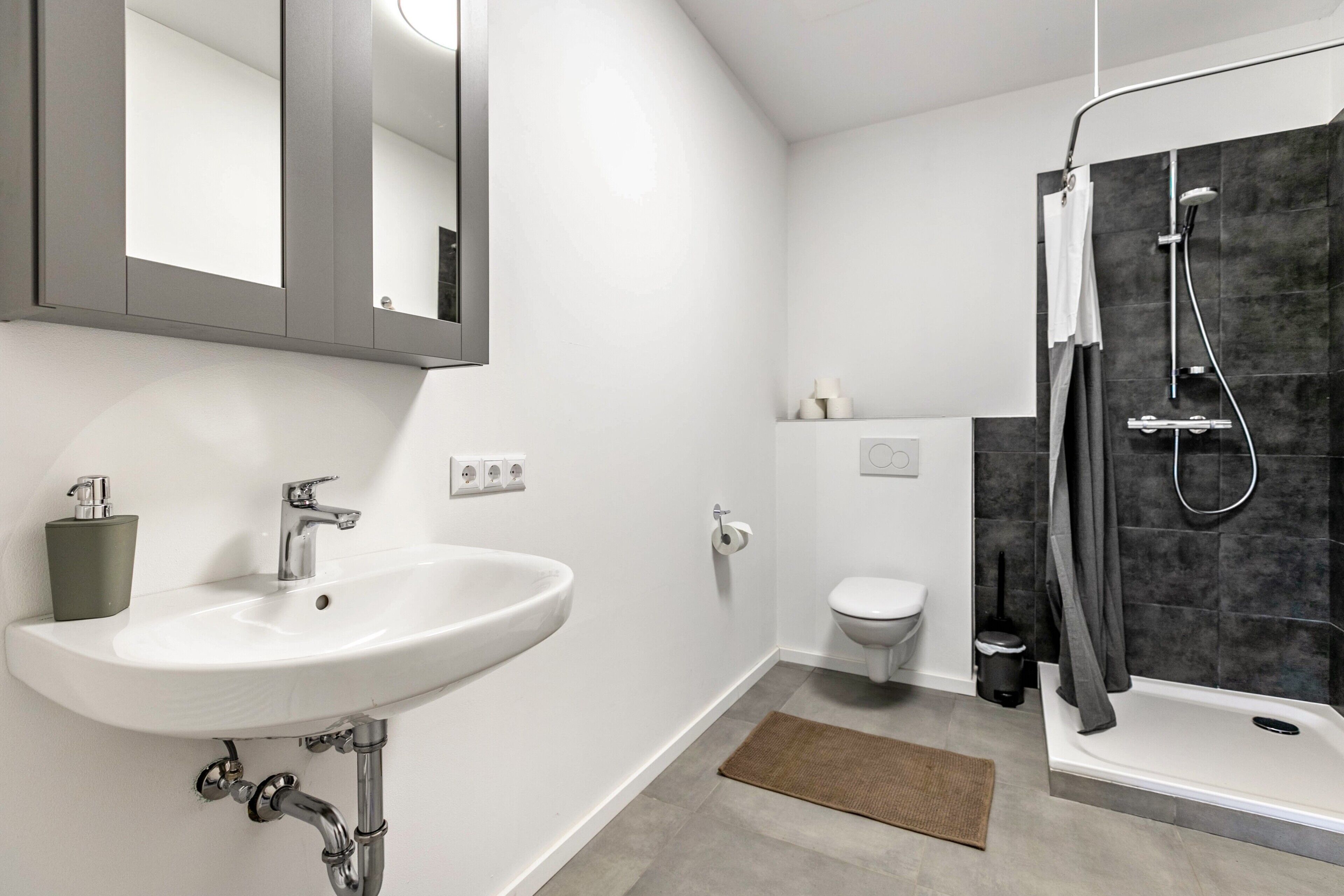 A modern bathroom with a white sink, mirror, toilet, and shower.