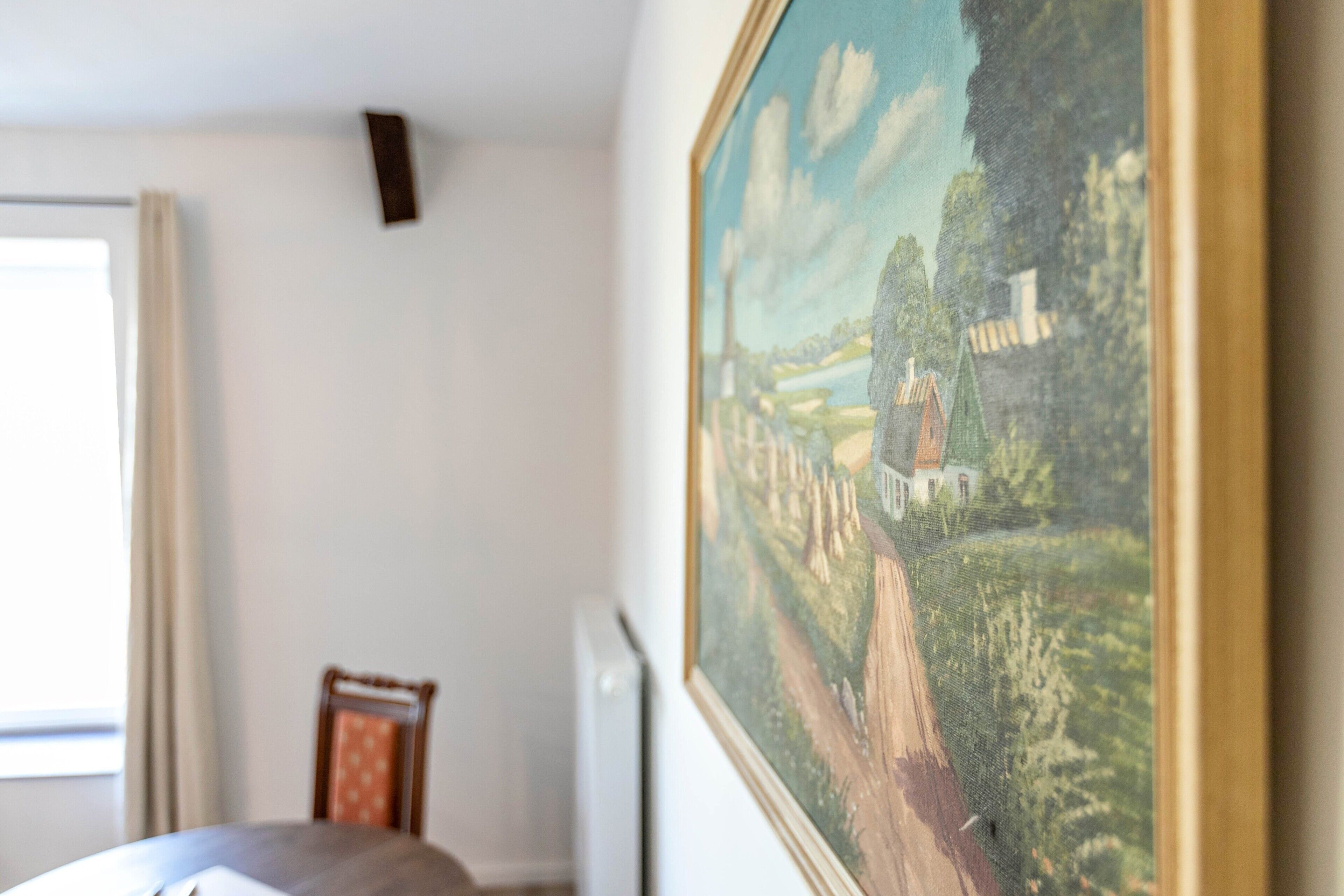 Ein Zimmer mit einem Bett, einem Sessel, einem Fenster mit Vorhängen und einem Bild an der Wand.