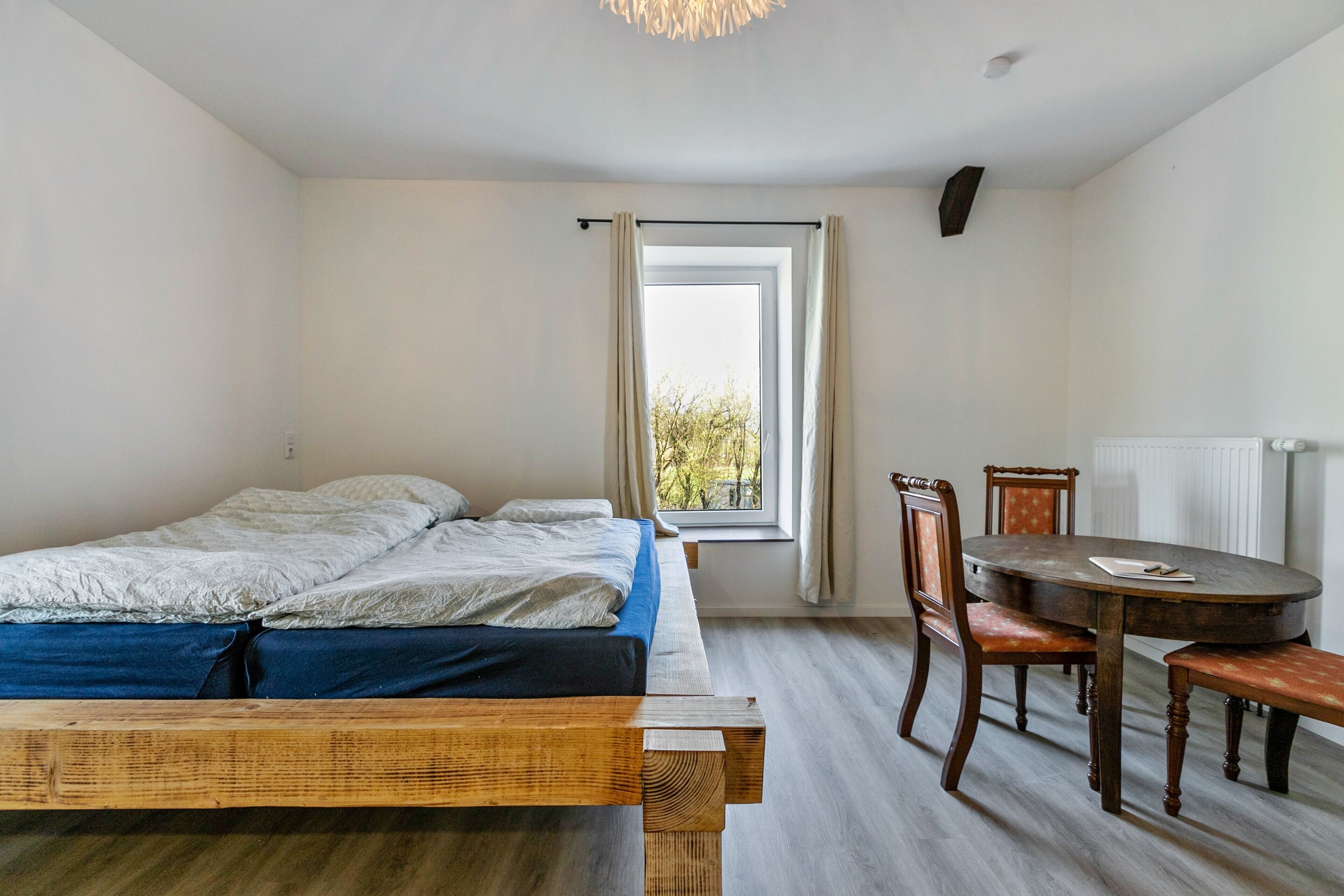 A bedroom with a bed, a dining table, chairs, and a window.