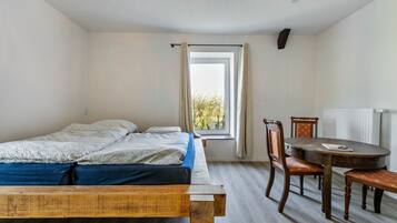 A bedroom with a bed, a dining table, chairs, and a window.